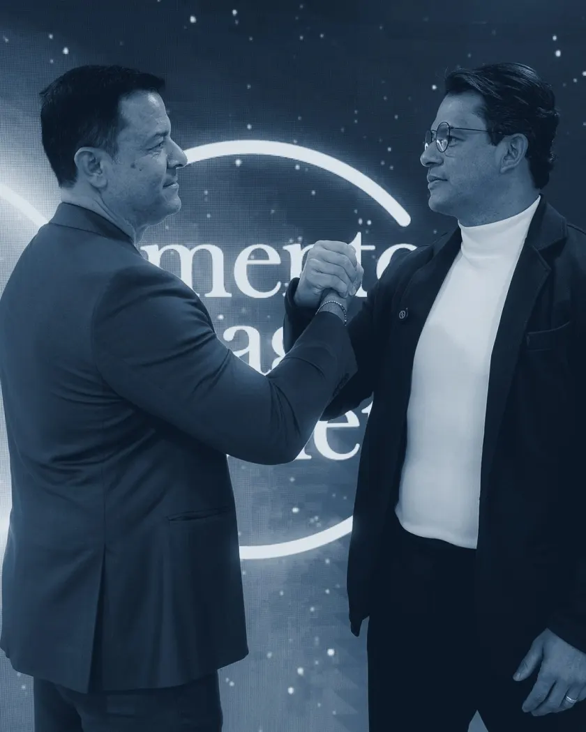 Waldo Souza e Alberto Machado em aperto de mão diante do painel da Mentoring League Society